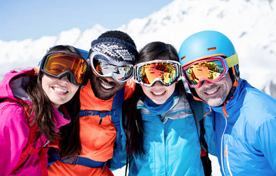 Four friends in colorful ski gear smiling together on a snowy mountain.